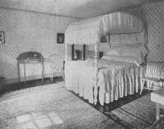 This bed-room is a good example of a simple Colonial
bed-room, and the rag rugs are in keeping with it. The repeat design of
the wallpaper ties the room into a unified whole.