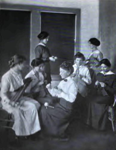 A Knitting Class at the Agricultural School. Note the
splendid poise of the Country Girl in the background, how naturally and
yet perfectly she is holding herself.